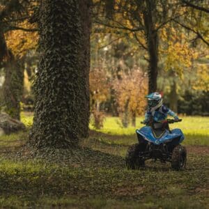 Дете кара синьо ATV през гората с есенни листа