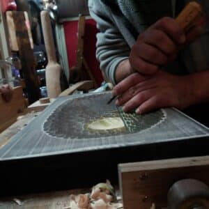 Ръце издълбават шарка върху дърво с длето.