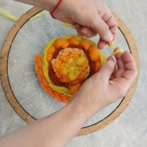 Ръце тъкат цветно пано с прежда върху дървен обръч.
