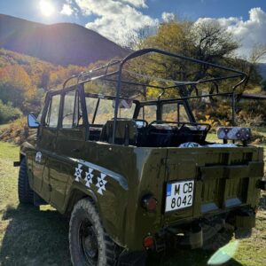 Военен джип на поляна с планина и слънце на заден план
